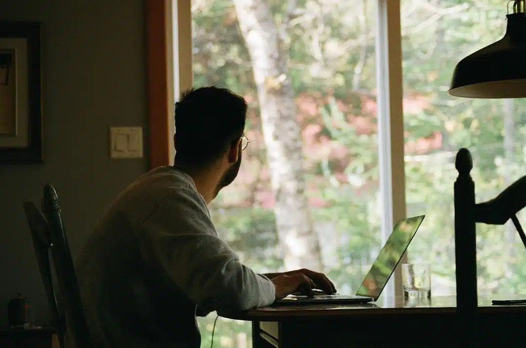 Man with laptop in home office looking out of window